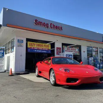 A red ferrari is parked in front of the smog check station.